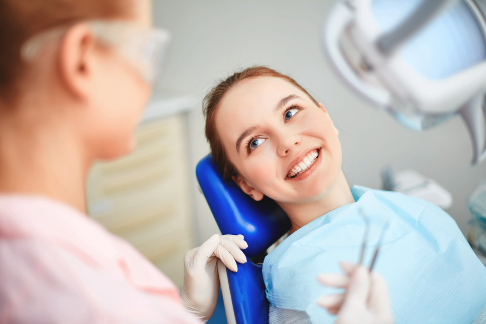 Young female sitting in dentist office and looking at her doctor with smile